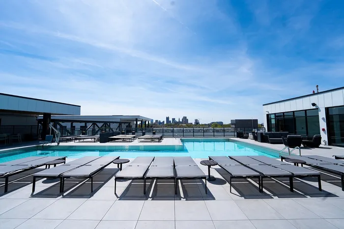 Luxurious rooftop pool area with sleek lounge chairs and stunning city skyline views under a clear blue sky.