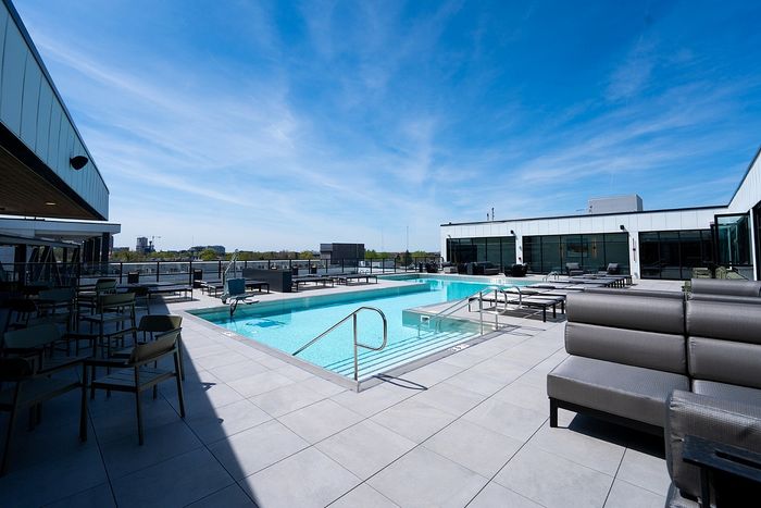 Luxurious rooftop pool with modern lounge chairs and panoramic city views under a clear blue sky.