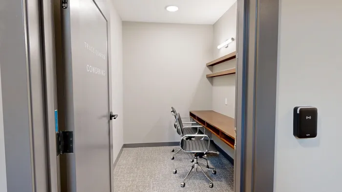 Modern coworking space with sleek design, featuring comfortable chairs and spacious desks under warm lighting.
