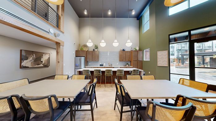 Modern community lounge with high ceilings, stylish pendant lighting, and an open kitchen area featuring sleek bar stools and ample dining space.