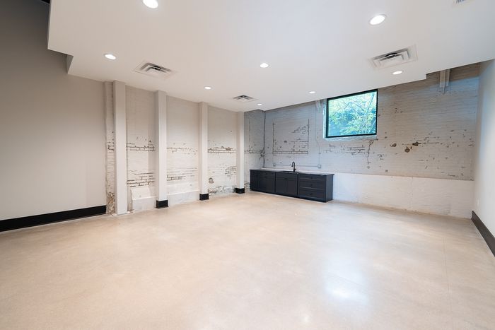 Modern spacious room with exposed brick wall, sleek black cabinetry, and ample natural light from a large window.