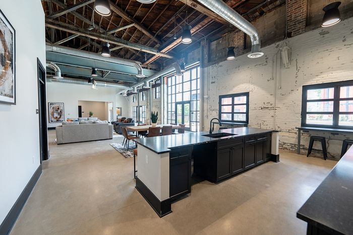 Chic industrial-style apartment featuring exposed brick walls, high ceilings, and modern open-concept living area with large windows.