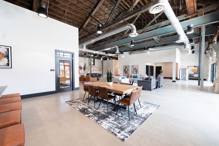 Spacious industrial-style loft with open-concept living area, stylish dining set, and cozy seating, featuring exposed beams and modern decor.