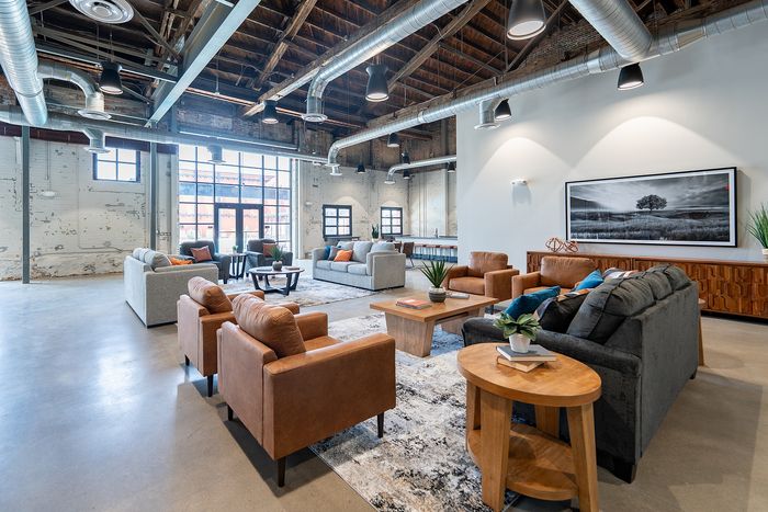 Stunning industrial-style living space with exposed ductwork, large windows, and modern furnishings in an open-concept design.
