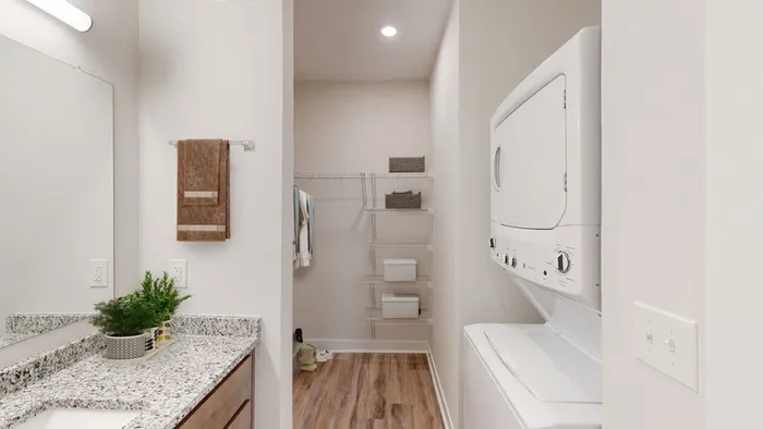Modern apartment laundry area with stacked washer and dryer, elegant granite countertop, and ample storage space.
