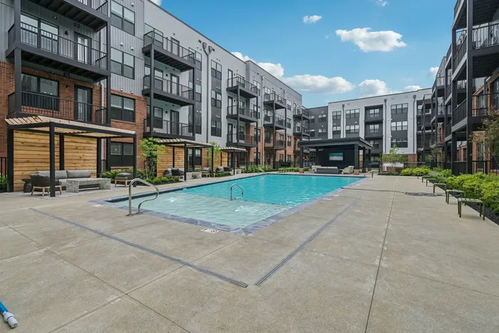 Luxurious apartment complex with a sparkling outdoor pool, stylish poolside cabanas, and modern balconies under a clear blue sky.