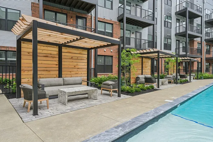 Modern apartment complex showcasing luxurious poolside seating with stylish pergolas and lush landscaping.