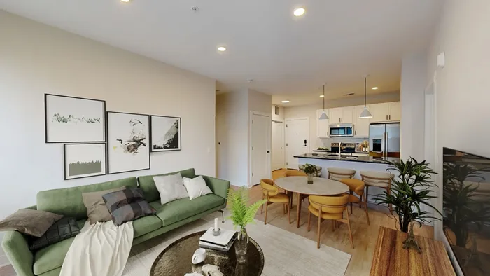 Modern open-concept living area featuring a stylish kitchen with stainless steel appliances, a cozy green sofa, chic dining space with elegant lighting, and contemporary decor.