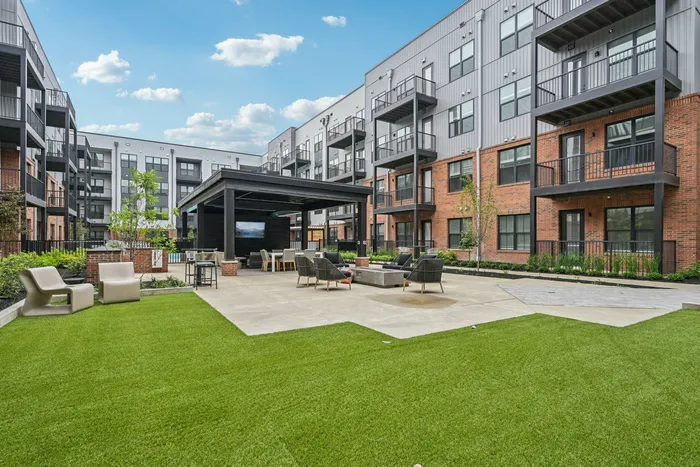 Modern apartment complex with a stylish courtyard, featuring lush green lawns, inviting seating areas, and contemporary architecture.