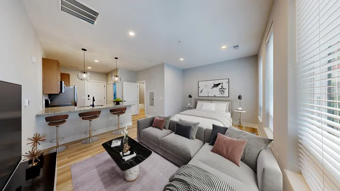 Modern and inviting studio apartment featuring a cozy bed, stylish living area with a plush sofa, and a sleek kitchen with pendant lighting and bar stools.