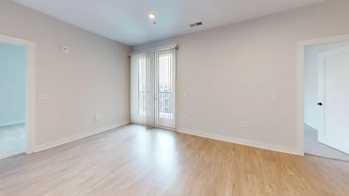 Bright, airy room with sleek wood flooring and large windows leading to a balcony, offering an inviting and versatile living space.