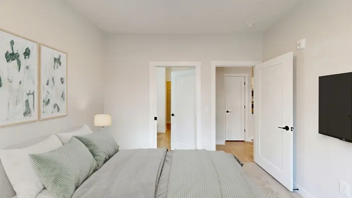 Cozy bedroom with modern decor, featuring soft green bedding and elegant wall art, opening into a bright hallway.