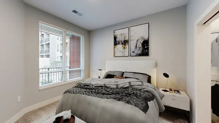 Modern bedroom with stylish decor, featuring a cozy bed, abstract wall art, and a large window with city views.