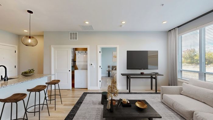 Bright and modern living room with elegant decor, featuring a cozy couch, sleek TV setup, and an inviting breakfast bar with stylish stools under chic pendant lighting.