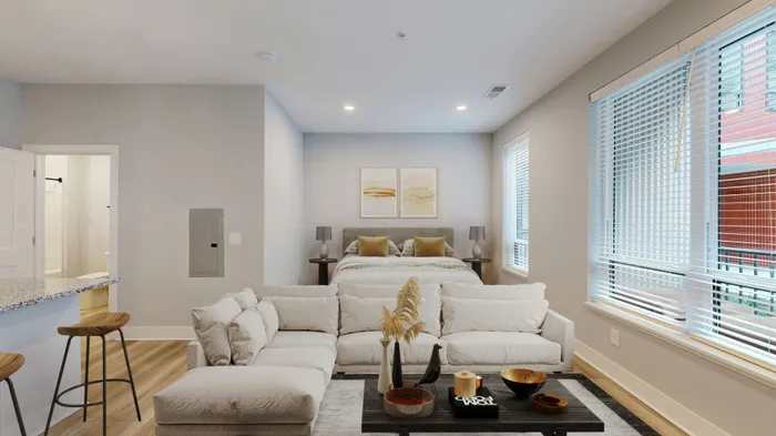 Chic studio apartment featuring a cozy living area, stylish kitchen bar stools, and a comfortable bed with elegant decor and ample natural light.