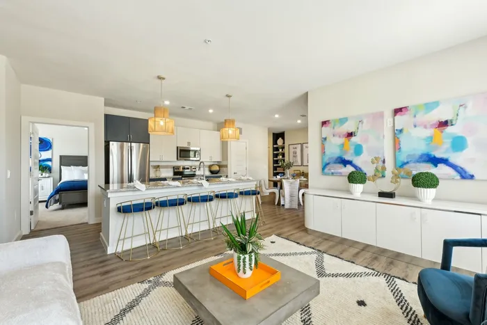Open-concept apartment with white walls, wood floors, a kitchen island with blue barstools, and blue and white cabinets