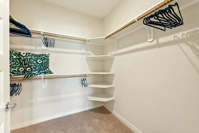 Walk in closet with built-in shelves in the corner, green pillows on the shelves, and blue hangers on the rack
