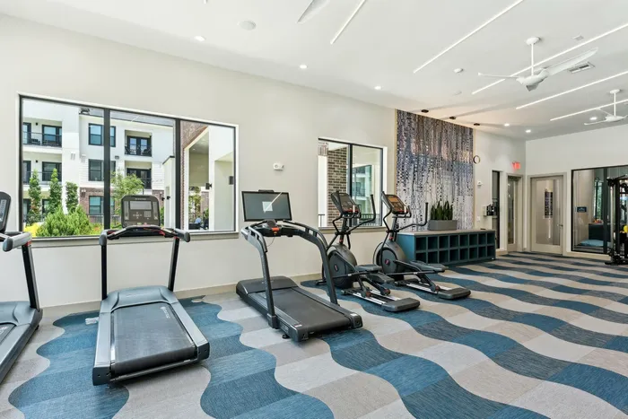 Wall of treadmills and elliptical machines overlooking an apartment courtyard through large windows