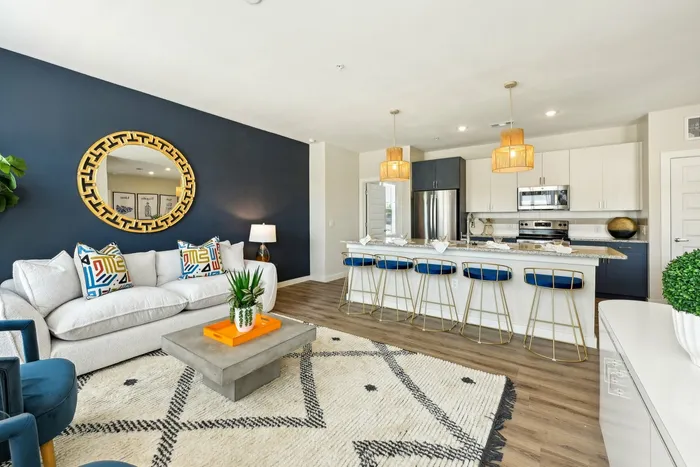 Apartment living room and kitchen with a blue accent wall, a kitchen island with blue barstools, and a white couch