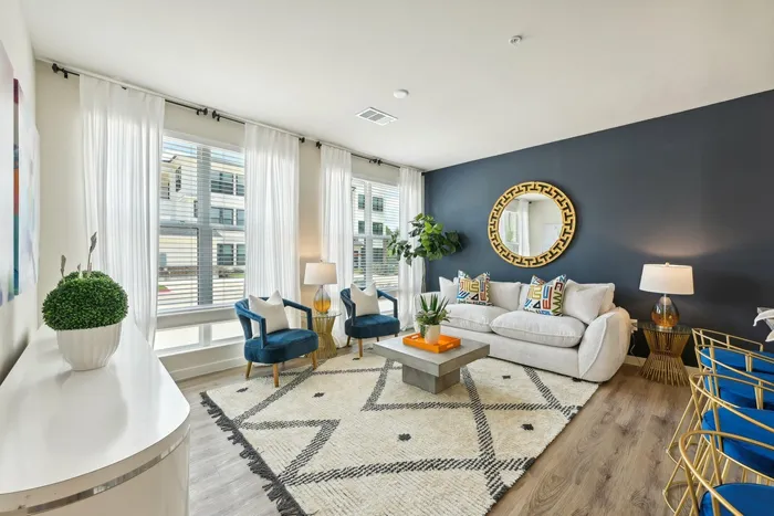 Living room with a blue accent wall, large windows with sheer white curtains, and blue chairs next to a white couch