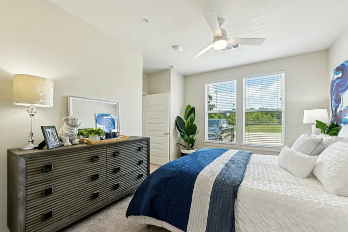 Bedroom with a white bed, blue blankets, and a dark wooden dresser with a lamp