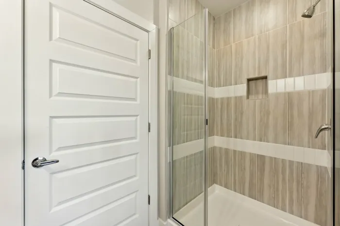 Walk in shower with brown and white tiles, next to a white closed door