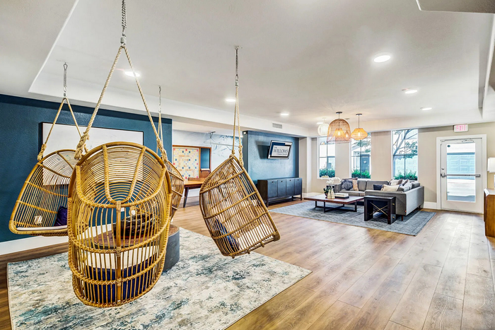 Stylish lounge area featuring hanging wicker chairs, modern decor, and a cozy seating arrangement on wooden flooring.