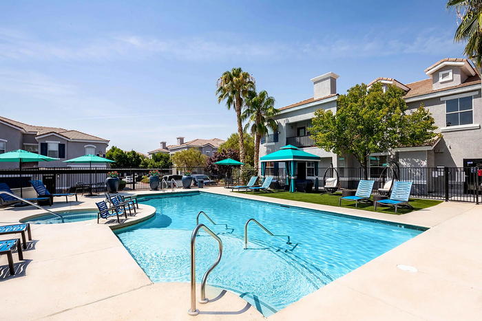 Stunning apartment complex pool area with sun loungers, palm trees, and vibrant umbrellas.