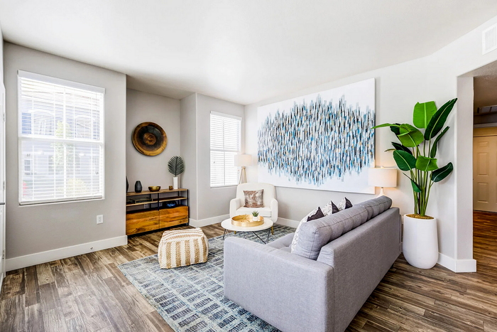 Bright and modern living room with stylish decor, featuring a large abstract painting, cozy seating, and potted plant in a sunny space.