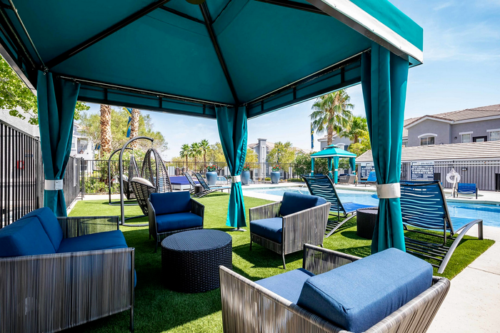 Luxurious outdoor seating under a cabana by the pool with modern chairs and lush greenery.