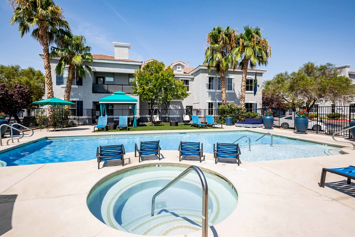 Inviting outdoor pool area with sun loungers, cabanas, and lush palm trees at a modern apartment complex.