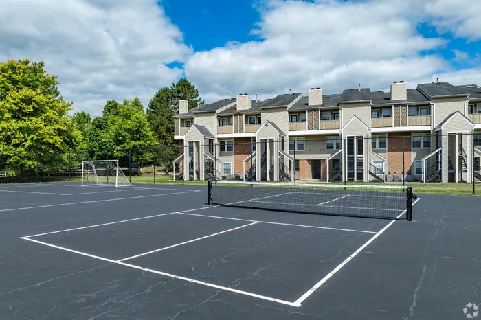 Charming apartment complex with a modern tennis and soccer court, surrounded by lush greenery and open skies.