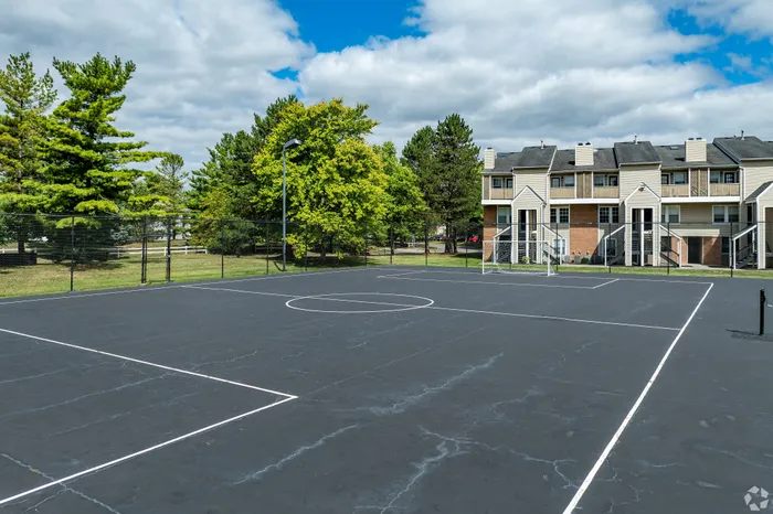 Expansive outdoor basketball court with adjacent modern townhouses surrounded by lush greenery.