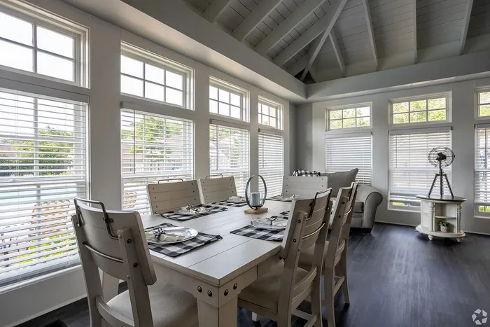 Bright and inviting dining area with elegant high ceilings, featuring a cozy table set for six near expansive windows that flood the room with natural light.