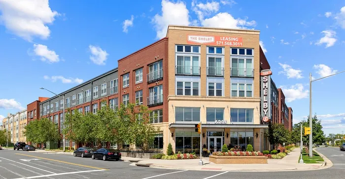 Modern apartment complex showcasing contemporary design with large windows, vibrant landscaping, and prime urban location under a clear blue sky.