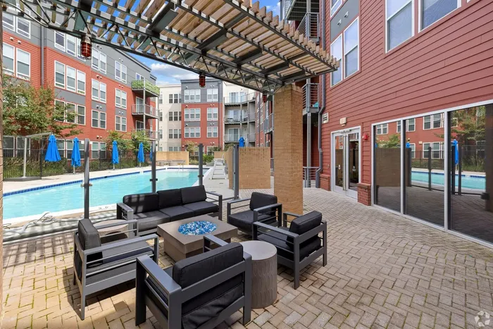 Modern apartment patio with stylish seating and a clear blue swimming pool, surrounded by vibrant red buildings and lush greenery.