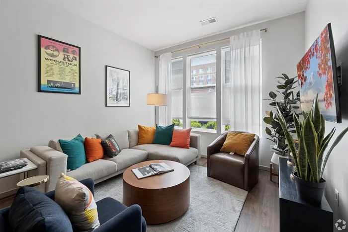 Bright and inviting living room featuring a cozy sectional sofa with colorful cushions, a stylish armchair, modern artwork, and large windows allowing natural light to flood in.