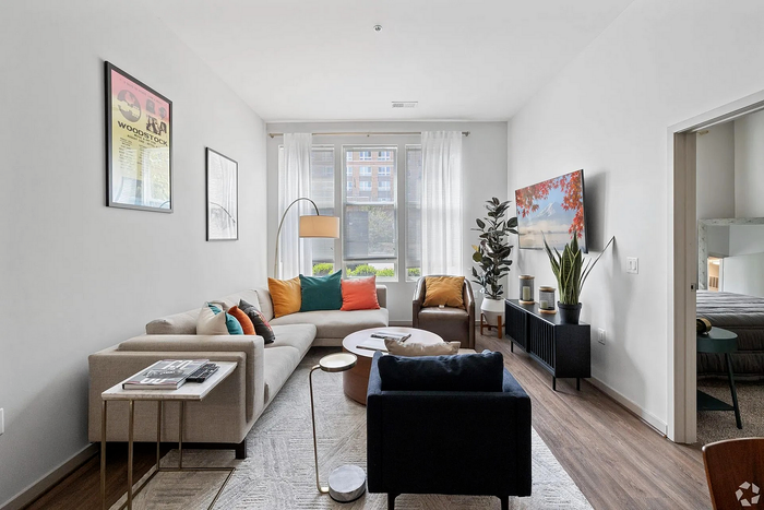 Bright and modern living room featuring a stylish sectional sofa, vibrant cushions, and a large window with natural light. Elegant decor with plants and art, suitable for a cozy urban lifestyle.