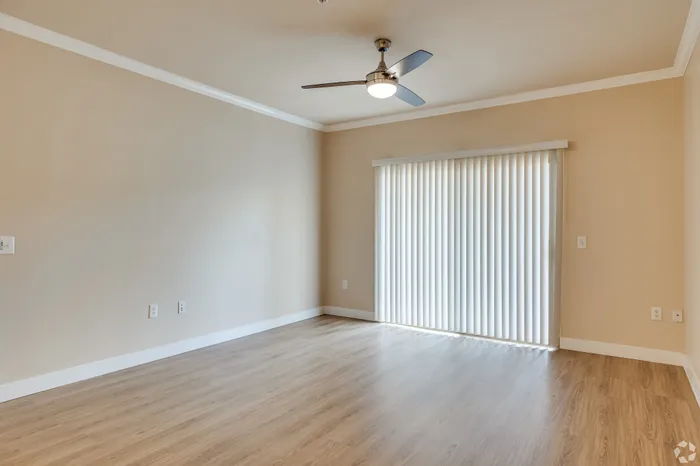 Bright and airy room with elegant wood flooring, stylish ceiling fan, and large sliding glass door with vertical blinds.