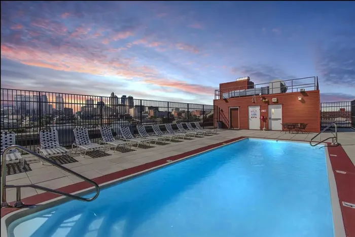 Breathtaking rooftop pool area with skyline view at sunset, featuring modern lounge chairs and vibrant sky.