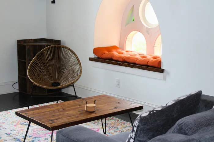 Chic apartment living space featuring a cozy orange window seat, stylish wooden chair, and rustic coffee table.