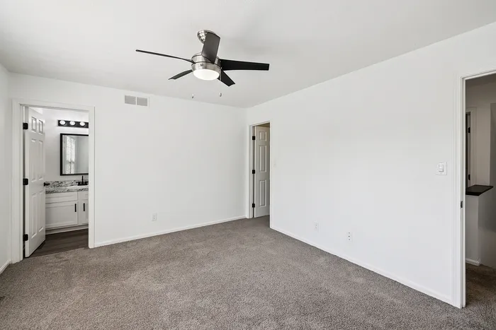 Bright, spacious bedroom with modern ceiling fan and plush carpeting, featuring a stylish en-suite bathroom.