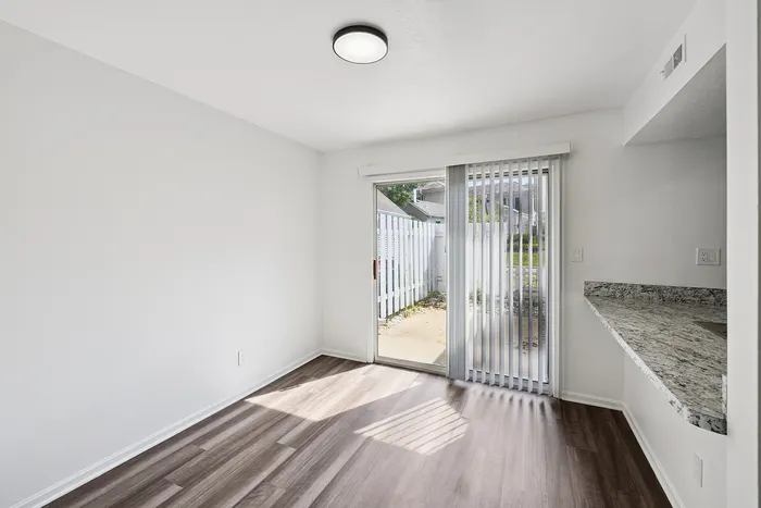 Bright and airy room with modern laminate flooring, sliding glass doors to a private patio, and a sleek granite countertop, perfect for stylish living.