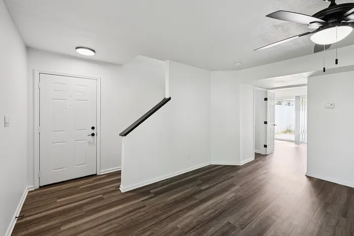 Inviting entryway with elegant dark wood flooring, fresh white walls, and a modern ceiling fan, leading to an open and airy living space with natural light.