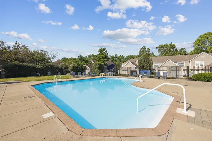 Inviting swimming pool area with sun loungers surrounded by charming townhouses and lush greenery under a clear blue sky.