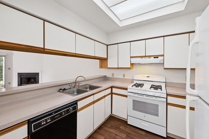 Bright and inviting kitchen with sleek white cabinets, modern appliances, and ample counter space, featuring a cozy view into the adjacent living area with a fireplace.