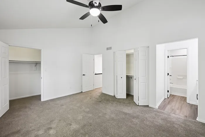 Modern bedroom with plush carpet flooring, elegant ceiling fan, spacious closets, and an adjacent bathroom entrance.