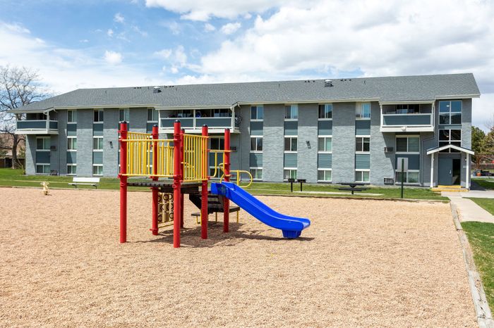 Charming apartment complex with a vibrant playground featuring a colorful slide, set against a backdrop of clear blue skies and green spaces.