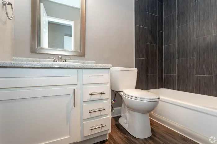 Modern bathroom featuring elegant dark tiled walls, sleek vanity with ample storage, and a clean, inviting bathtub.