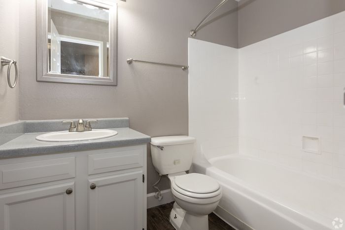 Bright and modern bathroom featuring a sleek vanity, elegant light fixtures, and a pristine bathtub with tiled walls.